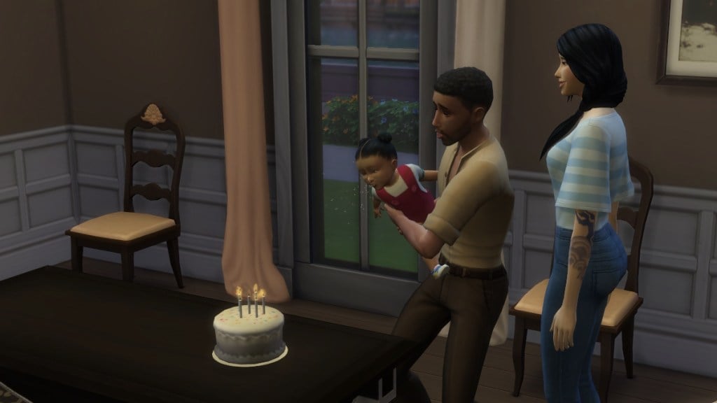 An adult male Sim holds his infant daughter as she leans in to blow out the candles on her birthday cake. Her mother looks on.