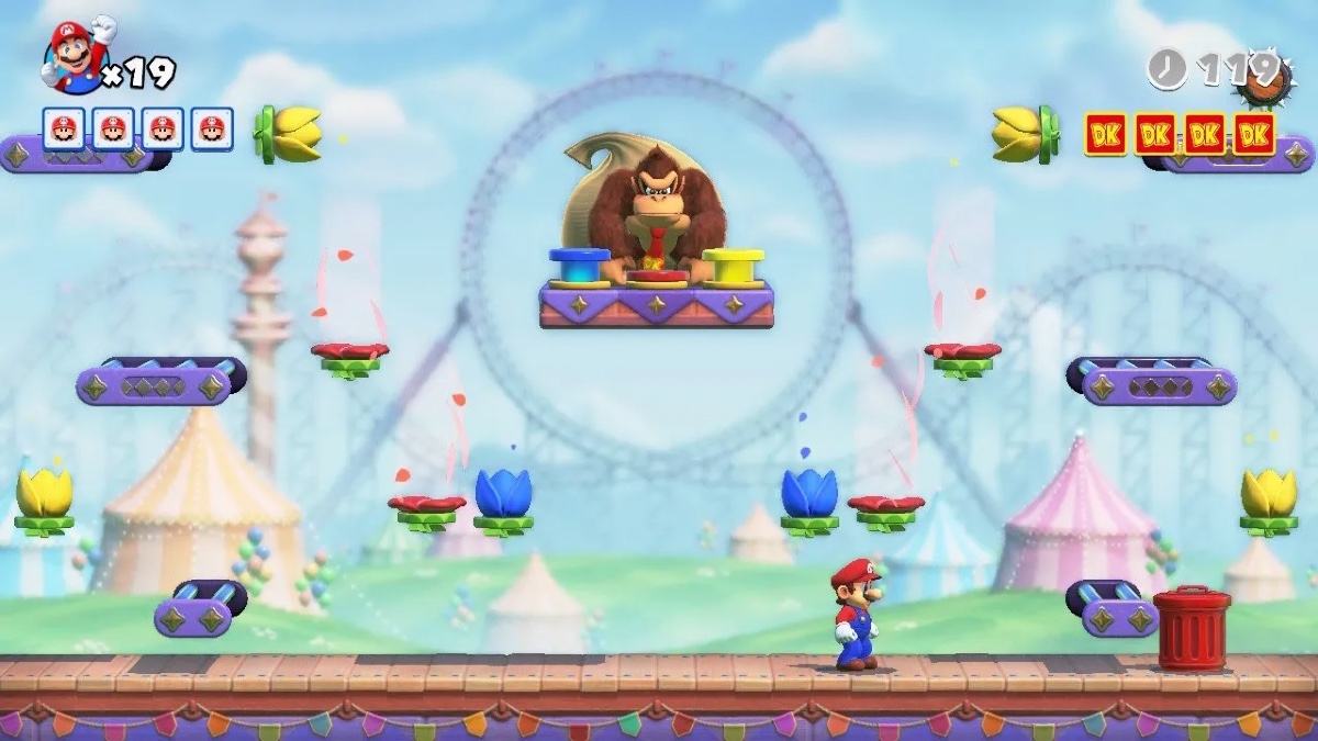 Mario stands and plots while a bored-looking Donkey Kong waits on a floating platform above him. Obstacles include flower-shaped fans. In the background, a pastel-colored scene featuring striped circus tents and a big looped roller coaster. 